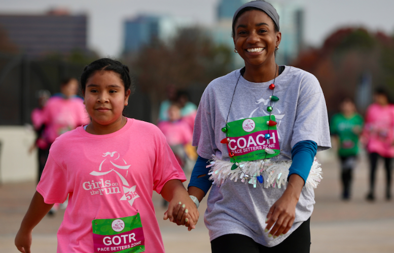 Coach and GOTR Girl smiling at the camera as they hold hands near the 5K finish